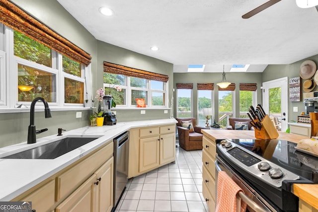 kitchen with decorative light fixtures, a skylight, sink, light tile patterned floors, and stainless steel appliances