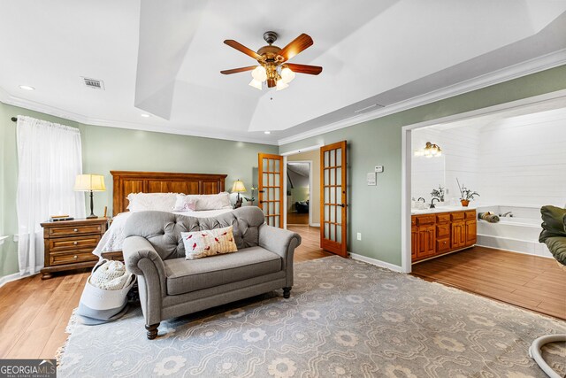 bedroom featuring ensuite bathroom, ornamental molding, light hardwood / wood-style floors, a tray ceiling, and french doors