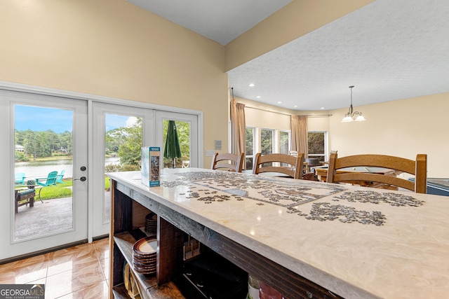 kitchen featuring hanging light fixtures, light tile patterned floors, a water view, a textured ceiling, and french doors