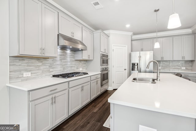 kitchen with sink, hanging light fixtures, ornamental molding, stainless steel appliances, and a center island with sink