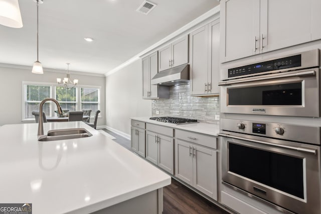 kitchen featuring sink, gray cabinetry, stainless steel appliances, a center island with sink, and decorative backsplash