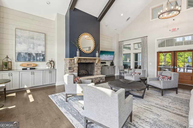 living room with an inviting chandelier, beam ceiling, wood-type flooring, a stone fireplace, and french doors