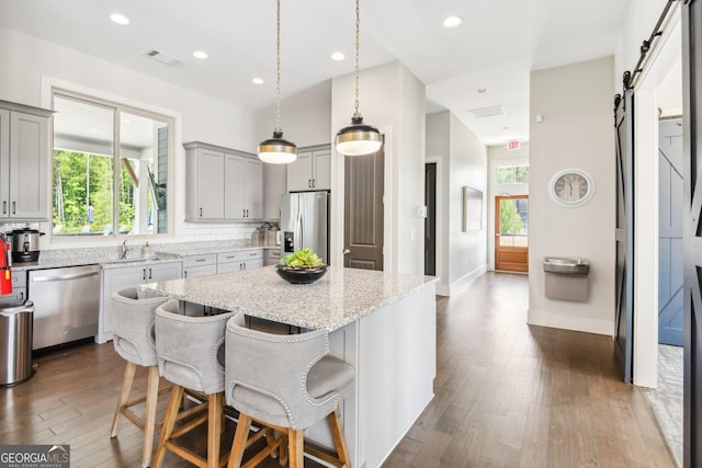 kitchen with a kitchen island, appliances with stainless steel finishes, a kitchen breakfast bar, light stone counters, and a barn door