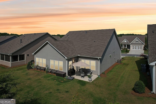 back house at dusk featuring a patio area and a lawn