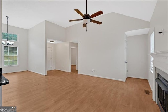 unfurnished living room featuring ceiling fan with notable chandelier, light hardwood / wood-style flooring, and high vaulted ceiling