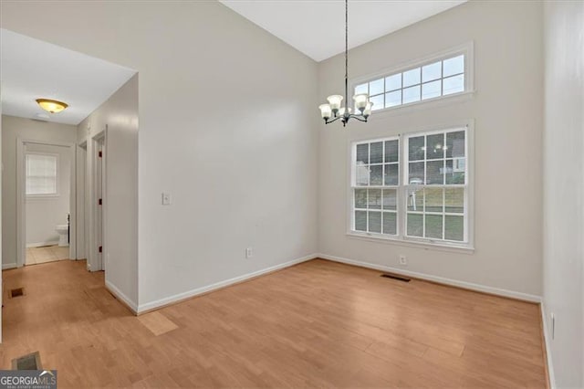 unfurnished room with a notable chandelier, light hardwood / wood-style floors, a healthy amount of sunlight, and a high ceiling