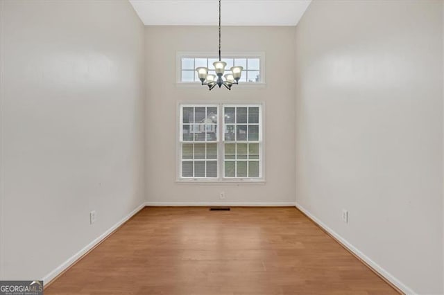 unfurnished dining area with a notable chandelier, baseboards, and wood finished floors