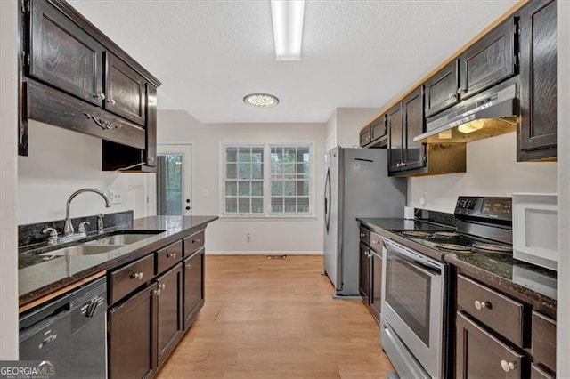 kitchen featuring appliances with stainless steel finishes, sink, dark stone counters, dark brown cabinetry, and light hardwood / wood-style flooring