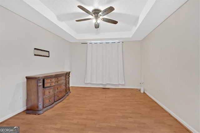 empty room featuring light hardwood / wood-style flooring, ceiling fan, and a tray ceiling