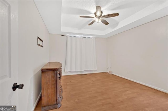 spare room featuring ceiling fan, a raised ceiling, light wood-style flooring, and baseboards