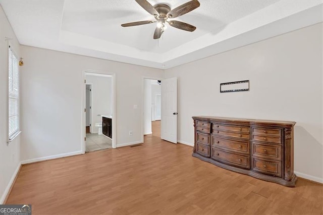 unfurnished bedroom featuring connected bathroom, a tray ceiling, light hardwood / wood-style flooring, and ceiling fan