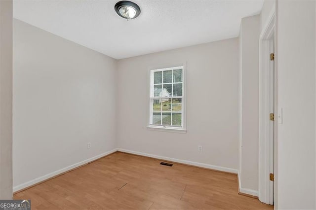 empty room featuring light wood-type flooring, visible vents, and baseboards