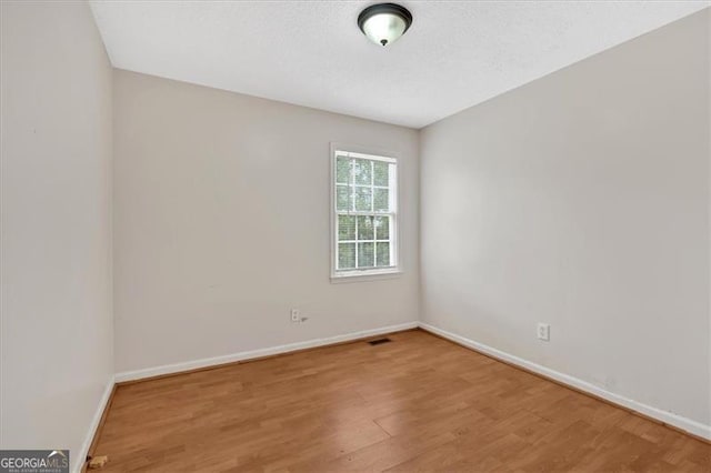 empty room featuring a textured ceiling, wood finished floors, visible vents, and baseboards