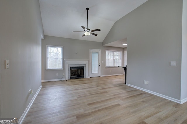 unfurnished living room with a high end fireplace, a wealth of natural light, light wood-style flooring, and baseboards