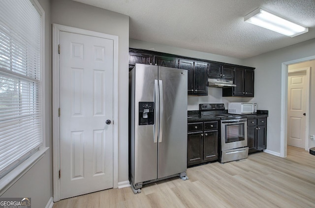 kitchen featuring dark countertops, appliances with stainless steel finishes, a textured ceiling, light wood-type flooring, and under cabinet range hood