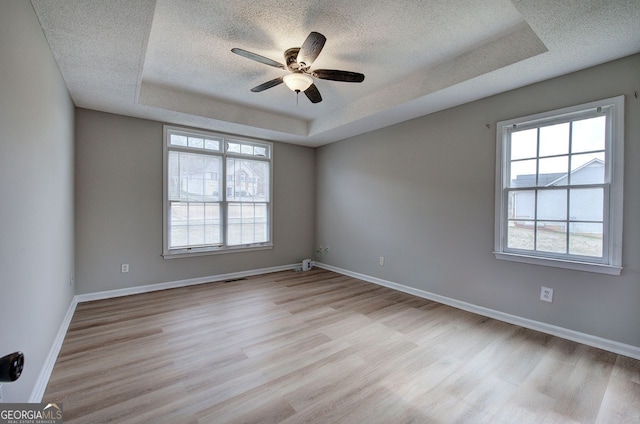 unfurnished room featuring light wood-style floors, baseboards, a tray ceiling, and a textured ceiling