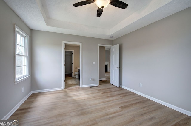 unfurnished bedroom featuring a tray ceiling, baseboards, a textured ceiling, and light wood finished floors