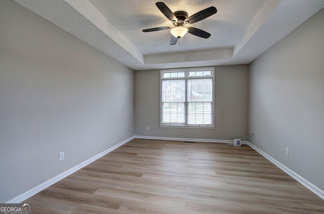 spare room with a tray ceiling, ceiling fan, a textured ceiling, wood finished floors, and baseboards