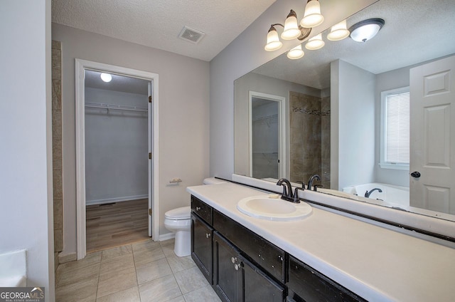 bathroom with a textured ceiling, toilet, visible vents, vanity, and a walk in closet