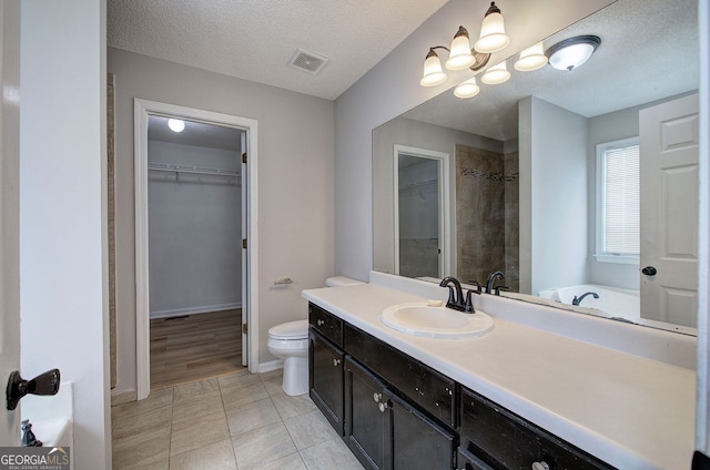 full bath featuring a textured ceiling, toilet, visible vents, vanity, and a spacious closet