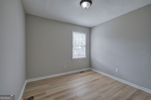 empty room featuring a textured ceiling, wood finished floors, visible vents, and baseboards