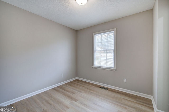 spare room with light wood-style floors, visible vents, and baseboards