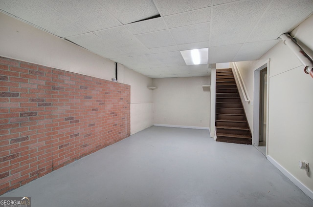 finished basement with a paneled ceiling, stairs, and baseboards