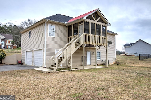 rear view of house with a sunroom, aphalt driveway, an attached garage, stairs, and a yard