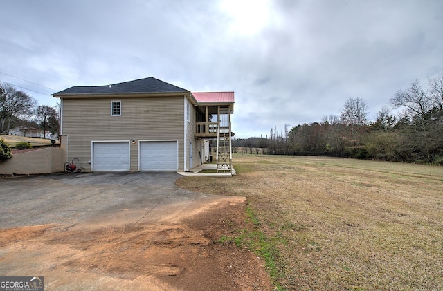 view of property exterior featuring a lawn, stairway, metal roof, aphalt driveway, and an attached garage