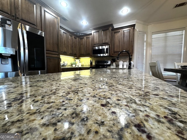 kitchen featuring sink, ornamental molding, stainless steel appliances, light stone countertops, and dark brown cabinets