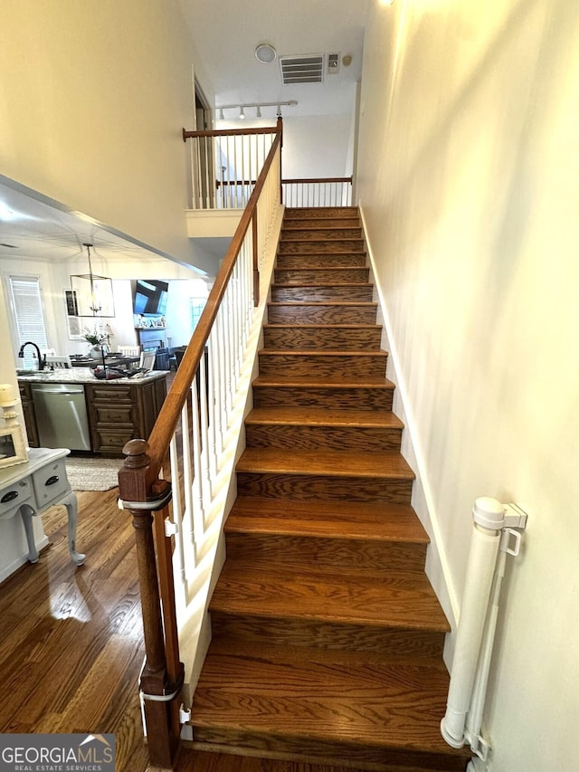 stairs with hardwood / wood-style flooring, rail lighting, and sink