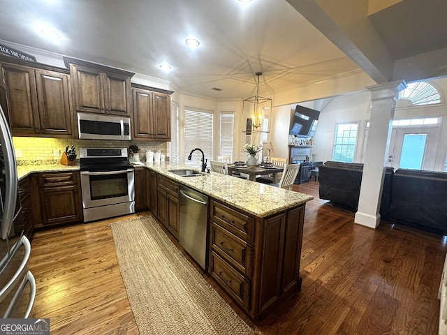 kitchen with sink, wood-type flooring, hanging light fixtures, stainless steel appliances, and decorative columns