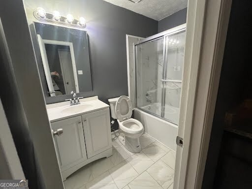 full bathroom featuring vanity, combined bath / shower with glass door, a textured ceiling, and toilet