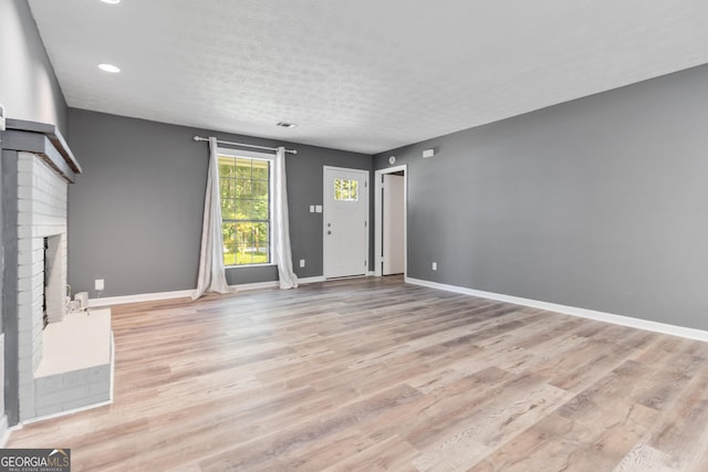 unfurnished living room featuring a fireplace, a textured ceiling, and light wood-type flooring