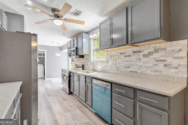 kitchen with sink, appliances with stainless steel finishes, light stone counters, washer / clothes dryer, and decorative backsplash