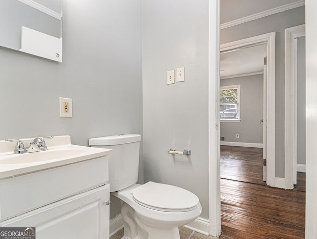 bathroom featuring toilet, wood finished floors, vanity, baseboards, and crown molding
