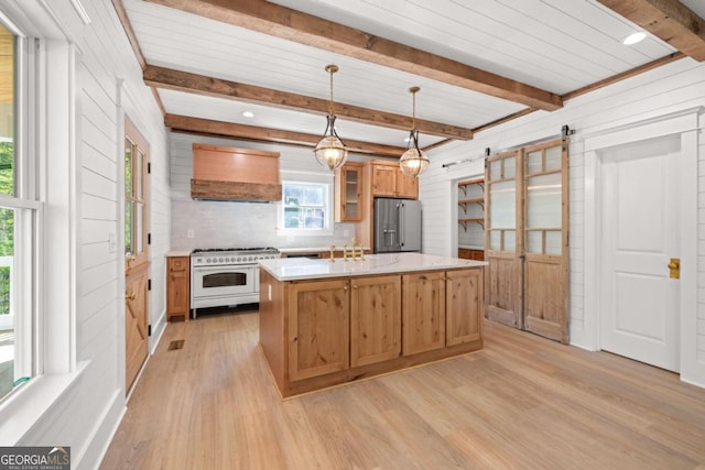 kitchen with pendant lighting, an island with sink, high end appliances, a barn door, and custom range hood