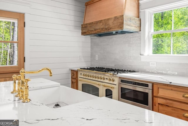 kitchen with oven, decorative backsplash, custom exhaust hood, double oven range, and light stone counters