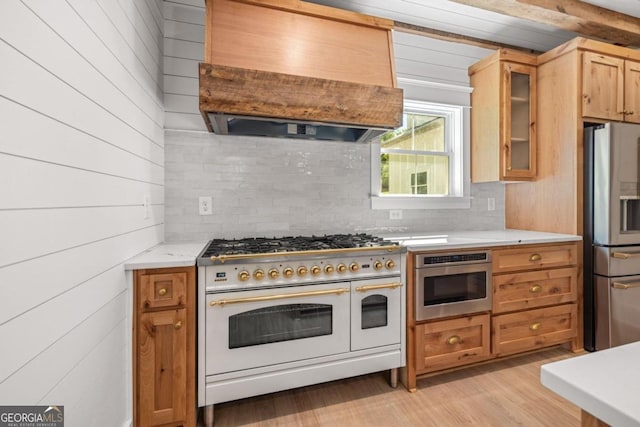 kitchen with appliances with stainless steel finishes, backsplash, wood walls, custom exhaust hood, and light wood-type flooring