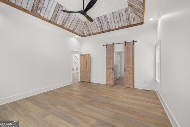 unfurnished bedroom featuring ceiling fan, a high ceiling, wooden ceiling, a barn door, and light wood-type flooring