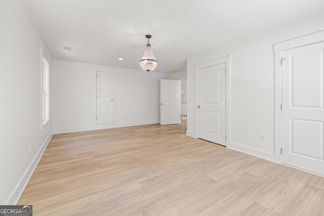 empty room with a chandelier and light wood-type flooring