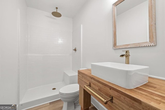 bathroom featuring a tile shower, hardwood / wood-style floors, vanity, and toilet