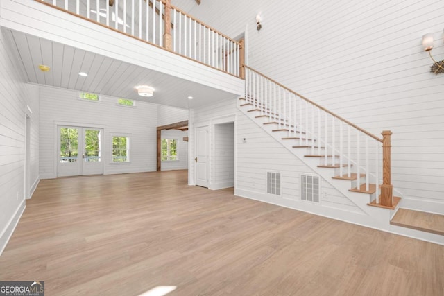 unfurnished living room with a towering ceiling, light hardwood / wood-style floors, french doors, and brick wall