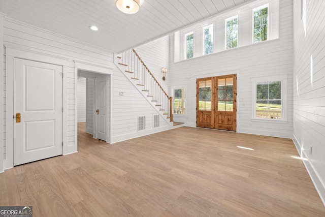 unfurnished living room featuring wood ceiling, a towering ceiling, and light hardwood / wood-style flooring