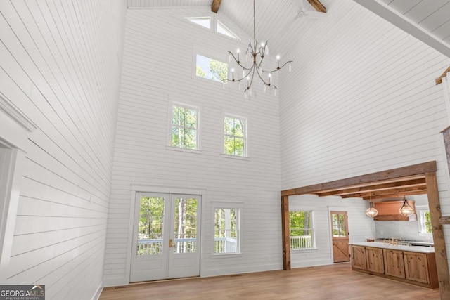 unfurnished living room featuring high vaulted ceiling, a notable chandelier, french doors, beamed ceiling, and light wood-type flooring