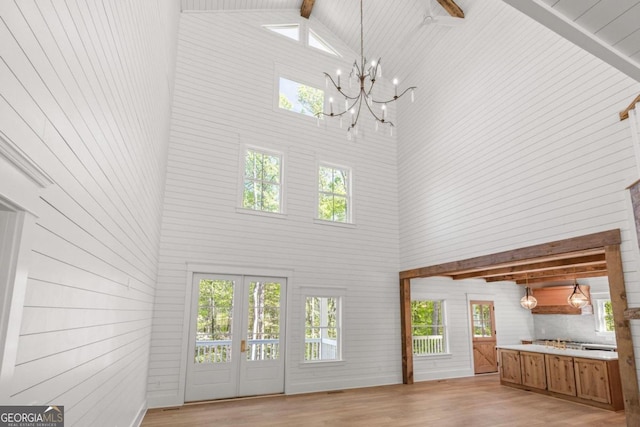 4226 Quail Creek Dr, Flowery Branch, GA 30542 - unfurnished living room featuring high vaulted ceiling, a chandelier, light wood-type flooring, healthy amount of natural light, and wood walls