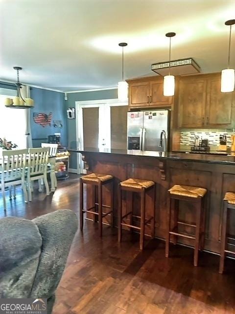 kitchen featuring pendant lighting, a breakfast bar, stainless steel fridge with ice dispenser, and tasteful backsplash