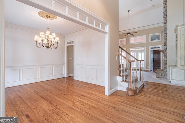 unfurnished dining area featuring ceiling fan with notable chandelier, light hardwood / wood-style flooring, ornamental molding, and a high ceiling