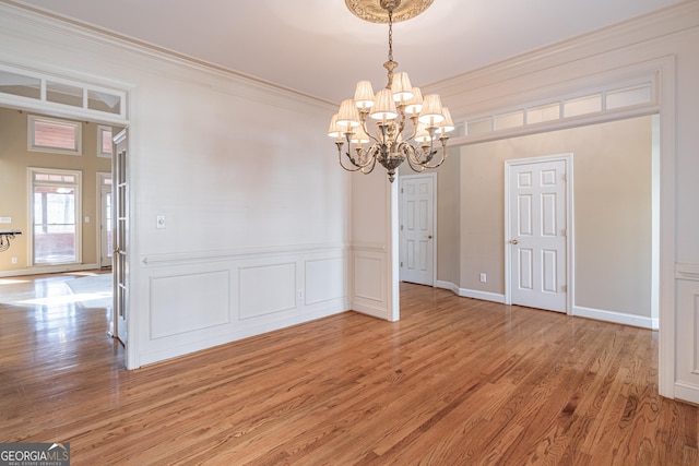 unfurnished dining area featuring wood-type flooring, ornamental molding, and a chandelier