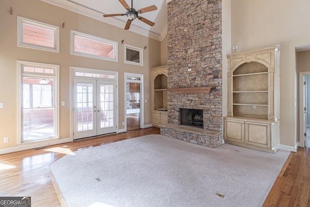 unfurnished living room featuring french doors, high vaulted ceiling, light wood-type flooring, ornamental molding, and a fireplace